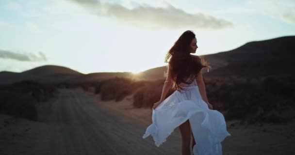 Mooie dame in een witte jurk bij zonsondergang op een geweldige plek in het midden van de natuur met een geweldig landschap rond — Stockvideo