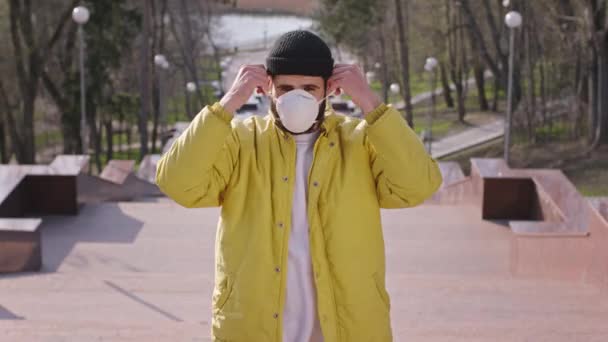 Молодой человек в жёлтой куртке и шляпе в защитной маске стоит на лестнице нового Ковид-19. 4k — стоковое видео