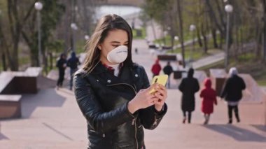 Yeni Coronavirus konseptindeki kadın, dışarıda, yüzünde koruyucu bir maskeyle telefonuyla arama yapmak için telefonunu alıyor.