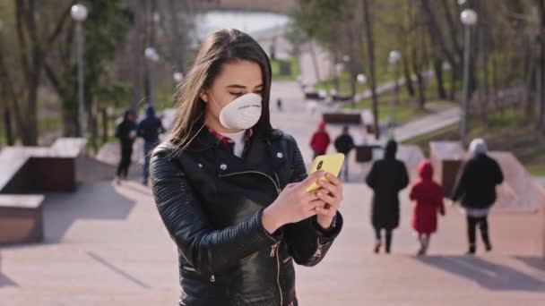 Nova senhora conceito Coronavirus tomando seu telefone para fazer uma chamada enquanto ela está fora ao lado do parque com uma máscara protetora em seu rosto — Vídeo de Stock