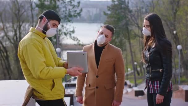 Друзі проводять час серед парку, одягнені в захисну маску, беруть електронну табличку, на якій щось друкують і аналізують час Коронавіруса. — стокове відео