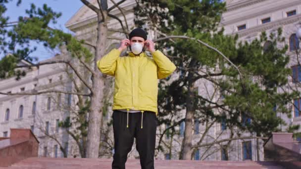 Молодой человек в жёлтой куртке перед камерой посреди пустой улицы снимает счастливую защитную маску после того, как карантин "Ковид-19" закончен. Снимок на ARRI Alexa Mini — стоковое видео