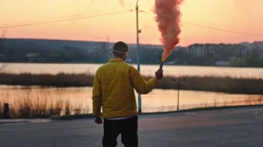Gün batımında parkın ortasında koruyucu bir maskeyle havadaki sis bombasını alıp Covid-19 Coronavirus 2019 'un kamera konseptine bakıyor.