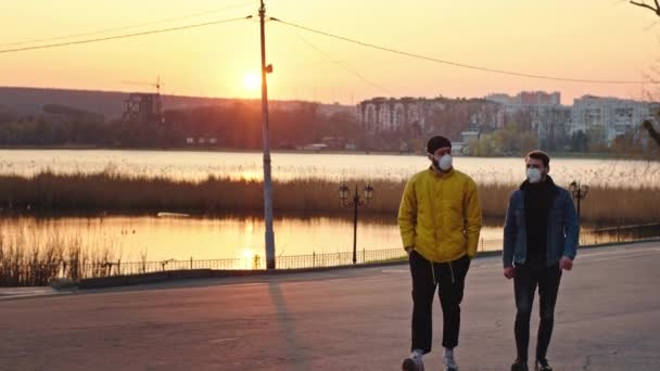 Чудові чоловіки, що йдуть перед камерою під час заходу сонця в парку, одягнені в захисну маску концепцію Коронавірусу мерців N1H1 — стокове відео