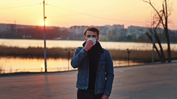 Un ragazzo che indossa la maschera protettiva in mezzo al parco vuoto al tramonto guarda dritto alla macchina fotografica nuovo tempo Covid-19 Coronavirus. Girato su ARRI Alexa Mini — Video Stock