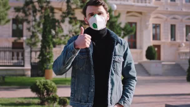 En man framför kameran utanför mitt på gatan bär en skyddande mask för Coronavirus mer han visar en stor så att det är viktigt att bära mask — Stockvideo