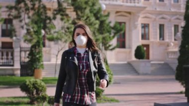 Caddede kameraya doğru yürüyen çekici bir kadın koruyucu bir maske takıyor ve Coronavirus 'la karantinada maske takmanın önemli olduğunu gösteriyor.