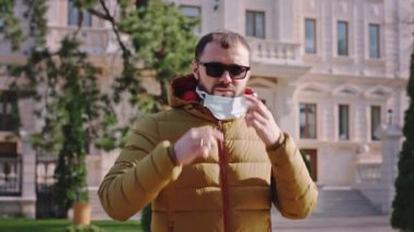 Kameramanın önünde koruyucu maskeyi al ve sokağın ortasında dikilirken yüzünü tak.