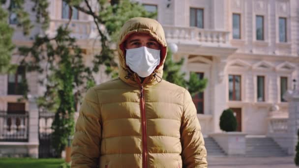 Харизматичный парень в маске и в пиджаке смотрит прямо в камеру посреди пустой улицы, в то время как карантин нового Ковид-19 — стоковое видео