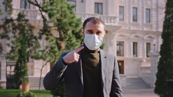 Framför kameran med en skyddande mask i ansiktet en kille som föreslår att bära masken medan det är en karantän av en ny Covid-19 — Stockvideo