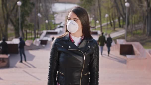 Kameranın önünde bir kadın doğrudan kameraya bakıyor koruyucu bir maske takıyor parkın merdivenlerinde duruyor yeni Covid-19 konsepti. — Stok video