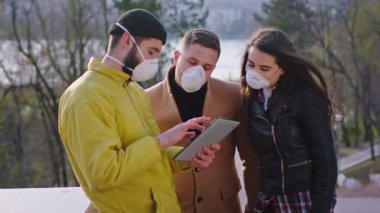 Parkın ortasında bir grup öğrenci koruyucu maskeyle birlikte elektronik tablet konsantre Coronavirus mermermerlerinin konseptine bakıyorlar.