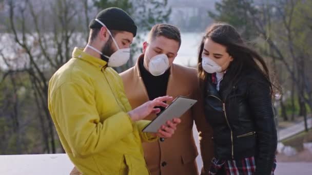 Groep studenten in het midden van het park in de quarantaine tijd met het beschermend masker ze kijken door de elektronische tablet geconcentreerde Coronavirus mers concept — Stockvideo