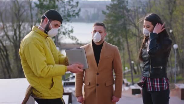 Coronavirus 2019 jonge groep vrienden hebben een leuke tijd samen in het park ze dragen beschermende maskers en neem een tablet om de statistieken van zieke mensen te analyseren — Stockvideo