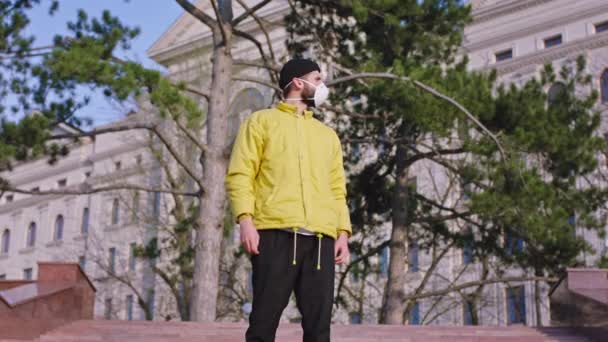 В жёлтой куртке парень, стоящий перед камерой посреди пустой улицы в карантине, носит защитную маску, концепцию коронавирусов. Снимок на ARRI Alexa Mini — стоковое видео