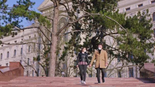 Couple charismatique devant la caméra au milieu de la rue vide portant le masque de protection et donnant un baiser à travers le masque, puis ils marchent dans la rue et regardant à partir de la — Video