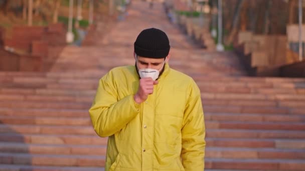 一般の人々で咳をしている外の若い男は、中国での彼の顔N1H1コロナウイルスのパンデミックに対する保護マスクを持っています。ARRIアレクサミニで撮影 — ストック動画