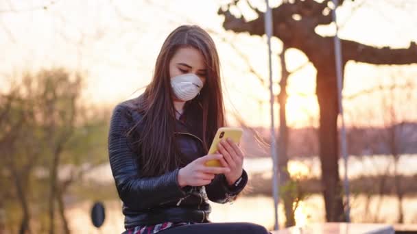 Dame charismatique dans le parc prendre son téléphone en tapant quelque chose tout en prenant un siège, elle est concentrée portant un masque de protection pour se protéger du nouveau Coronavirus Covid-19 — Video