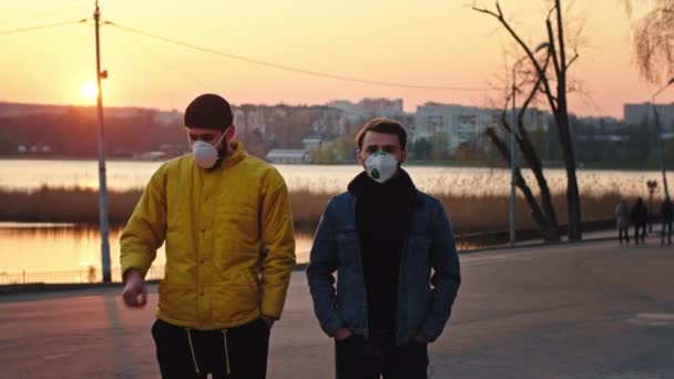 Στο ηλιοβασίλεμα στο πάρκο δύο φίλοι φορώντας την προστατευτική μάσκα στέκονται μπροστά από την κάμερα βήχουν ενώ κοιτάζουν κατευθείαν στην κάμερα N1H1 Covid-19 σε όλο τον κόσμο πανδημία — Αρχείο Βίντεο