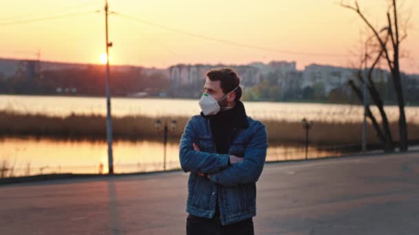 Uomo con una maschera protettiva in piedi davanti alla telecamera nel mezzo del parco vuoto al tramonto Covid-19 N1H1. 4k — Video Stock