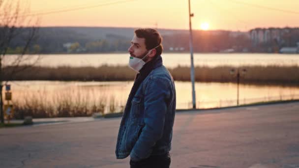 Concept de Coronavirus dans le parc vide au coucher du soleil quarantaine homme avec un masque de protection debout devant la caméra et regardant droit. Tourné sur ARRI Alexa Mini — Video