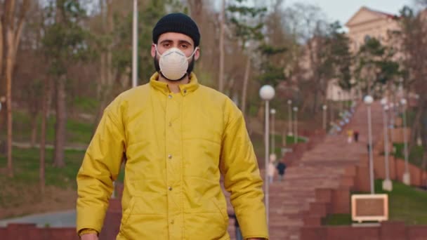 Voor de camera in het lege park man met een droevig gezicht en een beschermend masker op het gezicht recht naar de camera pandemie China N1H1 — Stockvideo
