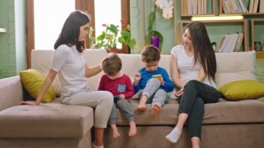 Çocuklar yeni Covid-19 karantinasında oyun oynarken çocukları kanepede oturan iki çekici anne.