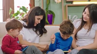 Kameraya yakın iki anne çocuklarıyla birlikte oynuyorlar. İki güzel çocuk akıllı telefonlarıyla oynuyorlar.