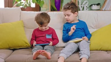 Kanepede otururken akıllı telefonu kullanarak komik bir şekilde sohbet eden iki küçük çocuğun portresi.