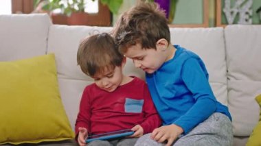 Güzel ve komik küçük çocuklar kameranın önünde kanepede otururken oyun oynamak için akıllı telefon kullanıyorlar.