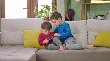 Evdeki iki sevimli çocuk kanepede oturuyor. Akıllı telefonu alıp birlikte oyunlar oynuyorlar. Birlikte eğleniyorlar.