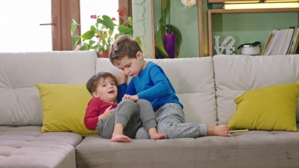 Dobrzy mali przyjaciele na kanapie dwoje dzieci spędzają razem zabawny czas grając w grę na smartfonie uśmiechają się duże — Wideo stockowe