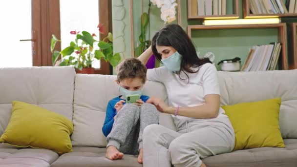 Karanténa čas doma mladá matka se svým dítětem sedí na pohovce ona urychluje čas se svým chlapcem, zatímco on pomocí smartphonu hrát novou Covid-19 koncept — Stock video