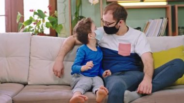 Kameranın önünde küçük bir çocuk babasıyla birlikte karantinada kalıyor koruyucu maske takıyor çocuk akıllı telefonu kullanarak kameraya büyük bir oyun oynuyor.