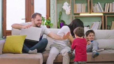 Oturma odasında çocuklarıyla birlikte güzel vakit geçiren genç bir çift gülümseyip oyun oynarken yeni Covid-19 karantinasında oturuyorlar.