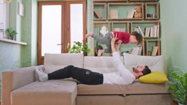 Mutlu karizmatik iki çocuk babalarıyla evde otururken oturma odasında kanepede eğleniyor.