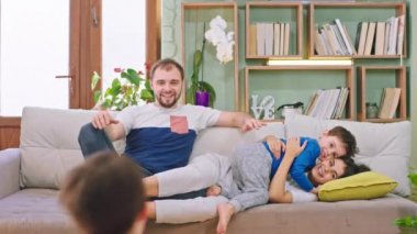 Mutlu ve gülümseyen genç bir aile. Küçük çocuklarıyla eğleniyorlar. Birbirlerine sarılıyorlar ve kamera önünde birlikte oynuyorlar.
