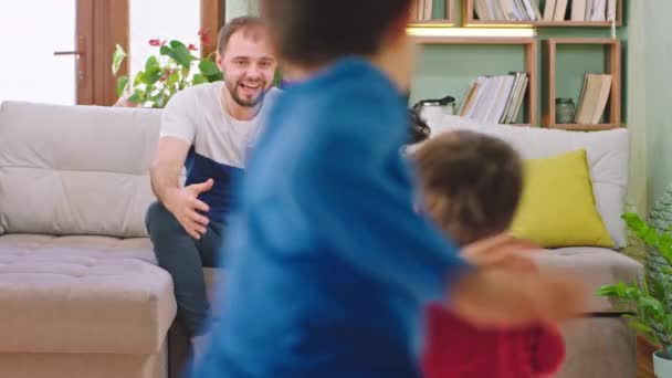 Jóképű szülők ülnek a kanapén, és boldogan ölelgetik a gyerekeiket. Mosolyognak, élvezik az együtt töltött időt, míg otthon maradnak. — Stock videók