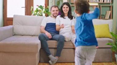 İki çocuk, genç ebeveynleriyle kanepede otururken eğleniyorlar. Çocuklar ailelerine koşuyorlar. Birbirlerine sarılıyorlar ve ailece vakit geçiriyorlar. ARRI Alexa Mini 'de çekilen