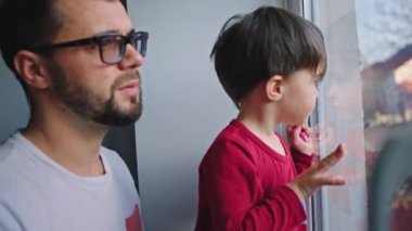 Kameramanın önünde, sevimli küçük oğlu pencereye bakarken evde, Coronavirus 2019 karantinasında.