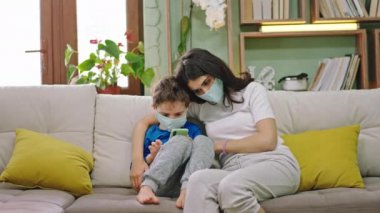 Bir anne ve küçük oğlu karantinada kalıyor koruyucu maske takıyorlar. Çocuk oyun oynamak için telefonu kullanıyor. Anne, yeni Coronavirus 2019 'a sarılıyor.