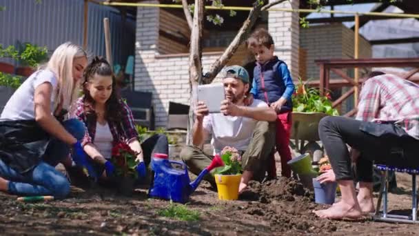 Dans une bonne journée ensoleillée grande famille à l'extérieur dans le jardin tous les membres travaillant ensemble la plantation de quelques fleurs sauver la nature un homme avec son fils prendre des photos d'autres travailleurs — Video