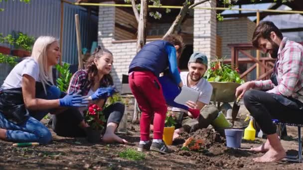 Spaß in einer großen Gesellschaft von Freunden im Garten pflanzen sie ein paar Blumen 5-jähriger Junge nehmen die Sprinkleranlage und gießen die Blumen, um schnell aufzuwachsen. 4k — Stockvideo