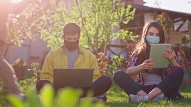 Bahçedeki ebeveynler tablet ve dizüstü bilgisayar kullanarak çalışırken oğulları Çin 2019 pandemisi Coronavirus 'un etrafında maske takıyor.