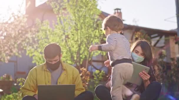 Bahçedeki çiftler çimlerin üzerinde otururken dizüstü bilgisayar ve tablet kullanıyorlar. Oğulları da güneş gözlükleriyle eğleniyor. Ailesinin ilgisine ihtiyacı var. — Stok video