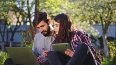 Çimlerin üzerinde temiz hava alan genç çift aletlerini alıyor ve dizüstü bilgisayar ve tablet kullanarak üniversite projesini birlikte yapıyorlar. ARRI Alexa Mini 'de çekilen