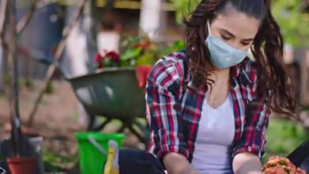 Pracující žena s ochrannou maskou a rukavicemi na zahradě se stará o květiny, je v karanténě doma koncept nové Covid19 pandemie — Stock video