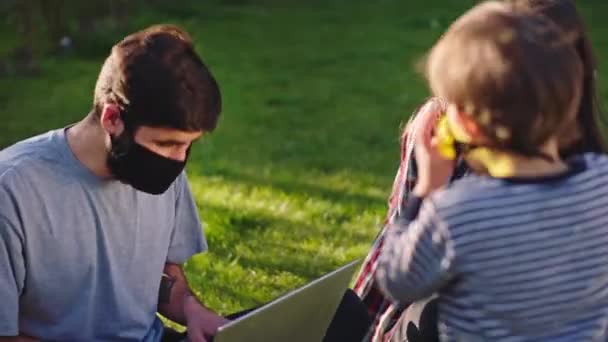 彼らはコロナウイルスパンデミックの彼らのかわいい息子の概念と遊んで隔離で保護マスクを身に着けている庭の両親と一緒に家にいます — ストック動画