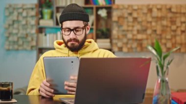 Ofisteki karizmatik adam aynı anda hem bilgisayarla hem tabletle uğraşıyor hem de kahve içiyor ve kendini mutlu ve rahat hissediyor.