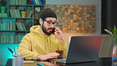 Çekici adam telefonuyla konuşurken bir şeyi açıklıyor. Evinden bilgisayarında çalışırken çok heyecanlı.